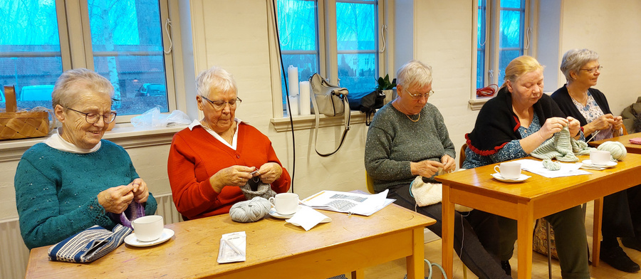 Kvinder strikker og drikker kaffe til et sognearrangement.