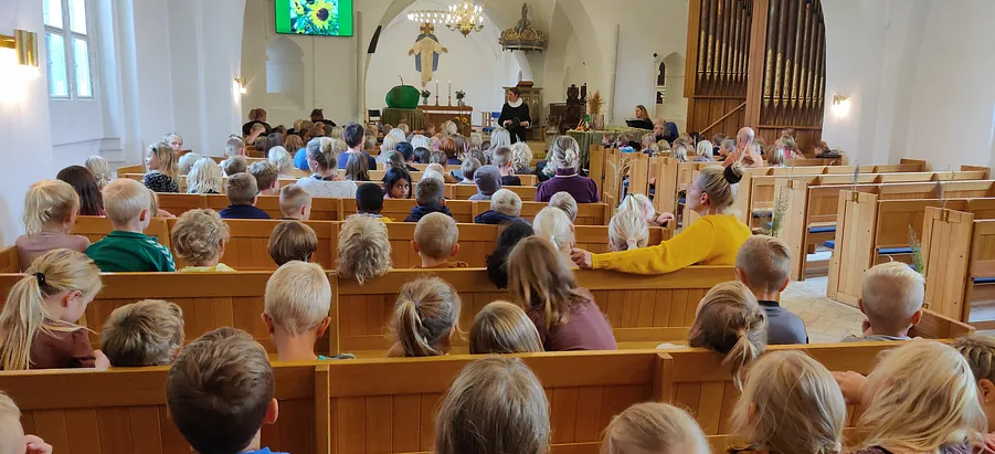 En gudstjeneste med børn i kirkebænke der ser præsten.