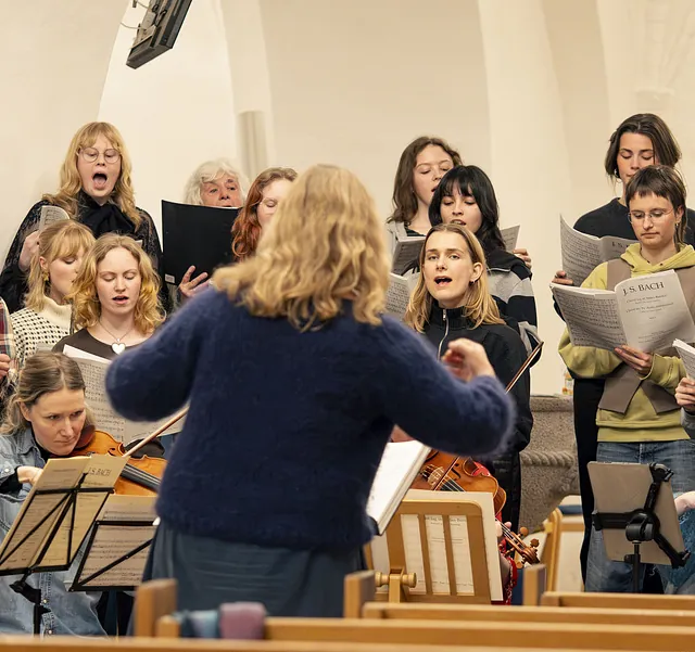 Dirigent leder kor og violinister ved en Bach-koncert i kirken.