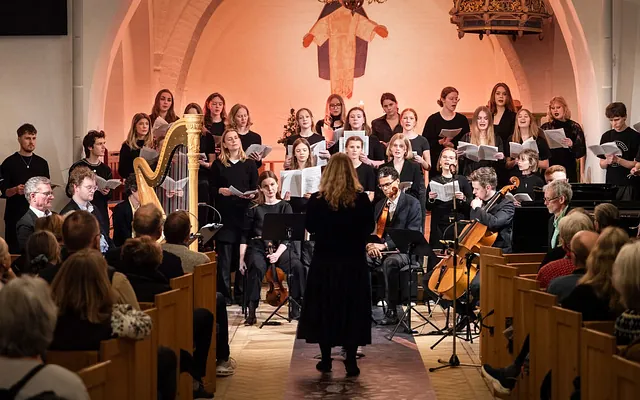 Kor og orkester med harpe opfører koncert i en fyldt kirke.