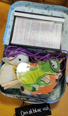 Åben aktivitetskuffert med bamse, krokodilledokke og instruktioner.