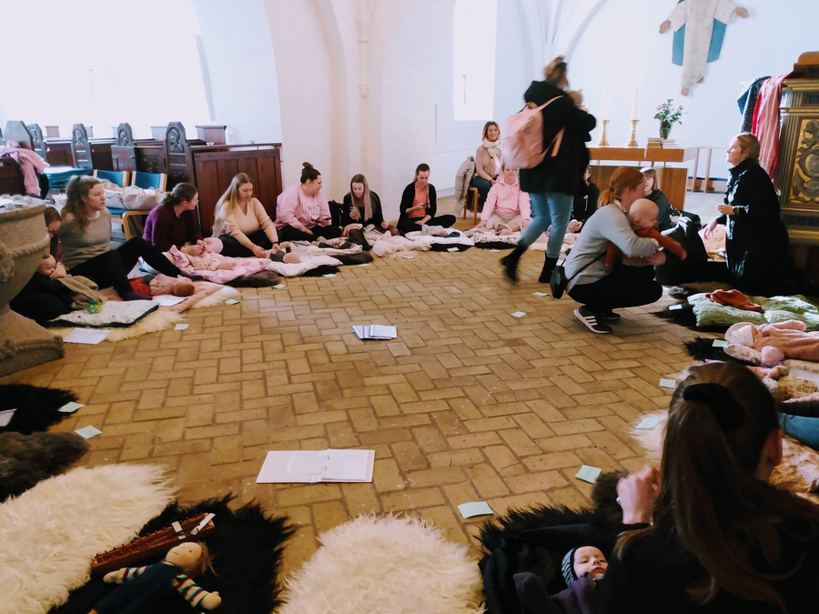En cirkel af mødre og babyer på måtter til babysalmesang i en kirke.